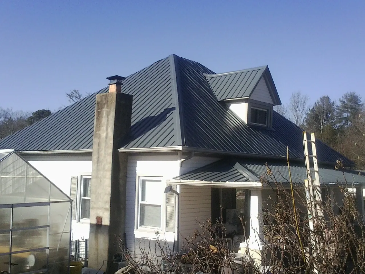 Dark blue standing seam metal roof on a white farmhouse with dormer — Slate & Tile Roof Repair by Roofing Brothers in Tintah