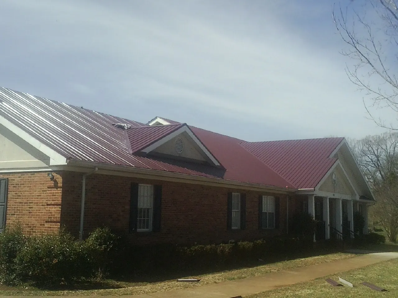 Red metal roof with gabled entries on a long brick building, from a Hail Damage Roof Repair job in Tintah