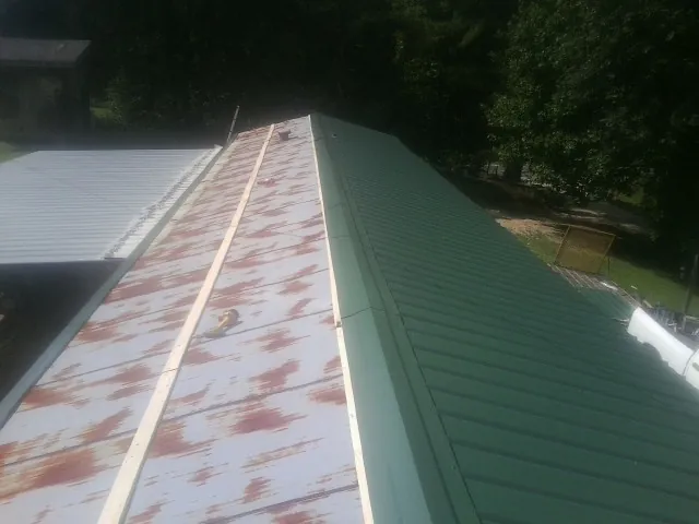 Old rusted panels beside newly installed green metal roofing — Wind Damage Roof Repair by Roofing Brothers in Tintah