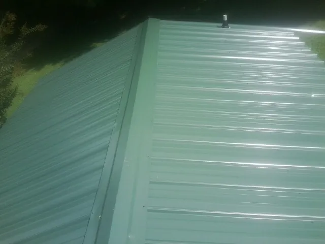 New green metal panels meeting at the ridge of a roof — Flat Roof Repair work by our crew in Tintah