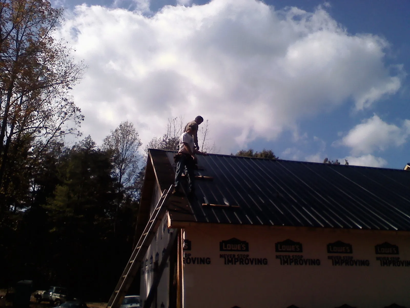 Roofer fastening dark metal panels high against a cloudy sky, from a Roof Inspection job in Tintah
