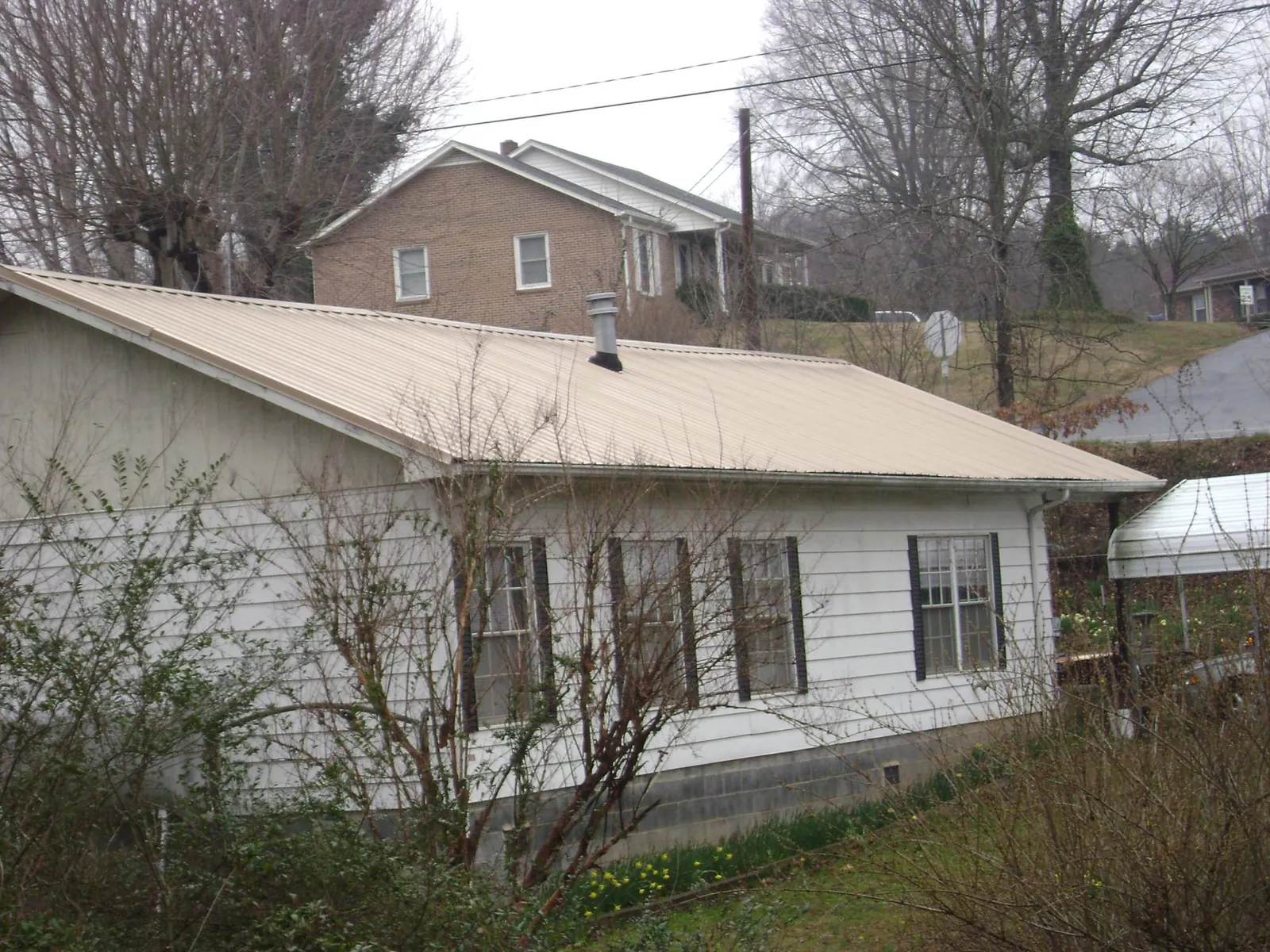 Tan metal roof on a white sided house set into a hillside — Commercial Roofing by Roofing Brothers in Tintah